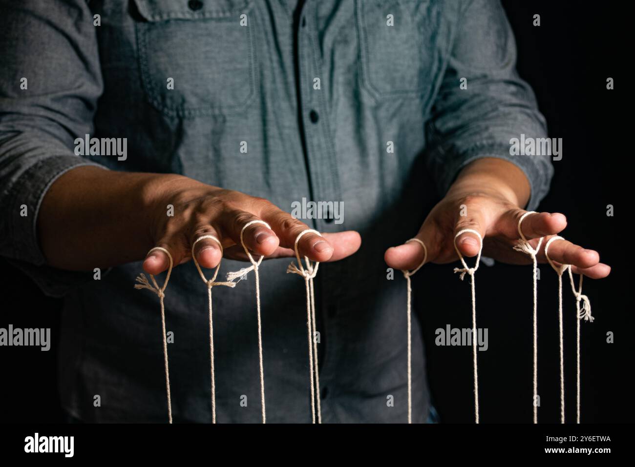 Close-up Of Man Controls The Puppet With Fingers. Man`s Hand Controls The Puppet With The Fingers Attached To Threads Against Black Background,Manipul Stock Photo